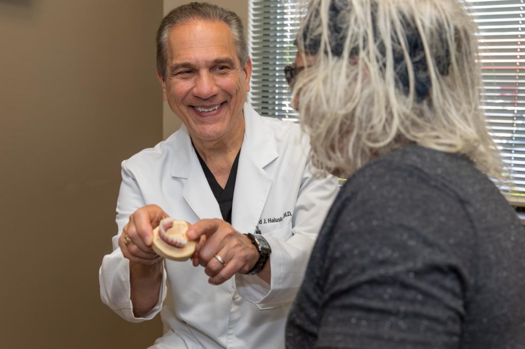 oral surgeon dr halusic showing a dental implant model to older male patient