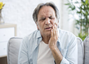 a man in discomfort, holding his jaw because of dental implant pain