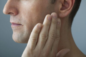 a picture of a patient holding his jaw where he needs a tmj treatment.