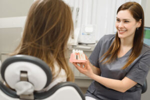 a picture of an oral surgeon showing a patient a dental implant model before her dental implants are accurately placed with CHROME GuidedSMILE technology.