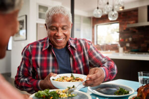 an older man smiling as he eats his dinner at the dinner table because an experienced oral surgeon improved his smile with dental implants.