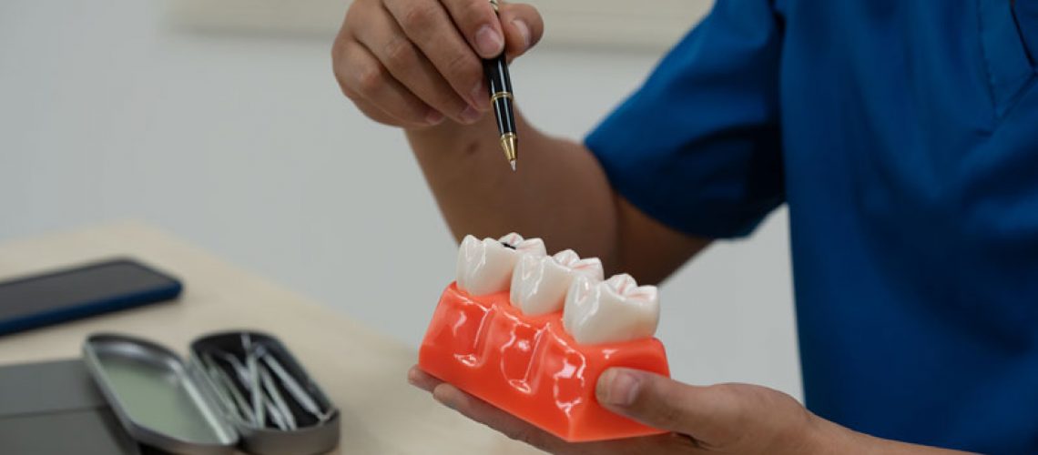 A male doctor sits working at the table in a dentist's clinic, explaining tooth decay, wisdom teeth, broken teeth, false teeth, and recommended treatments to patients.
