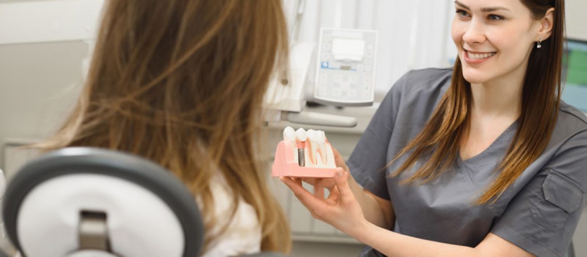 a picture of an oral surgeon showing a patient a dental implant model before her dental implants are accurately placed with CHROME GuidedSMILE technology.