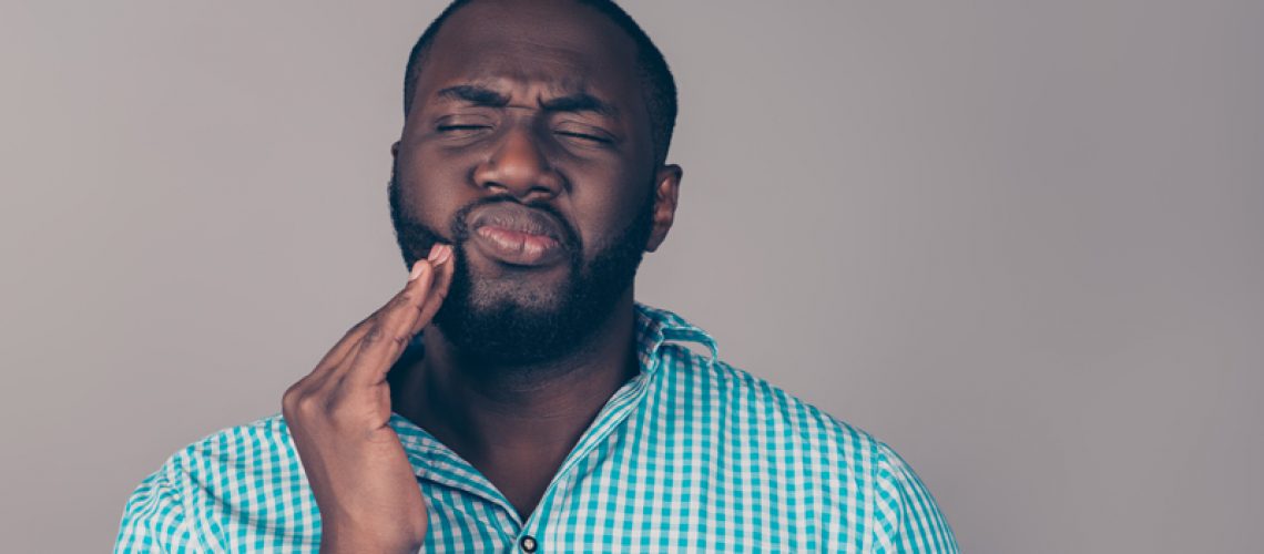 Photo of a dental patient holding his mouth in the spot of his troubled wisdom teeth